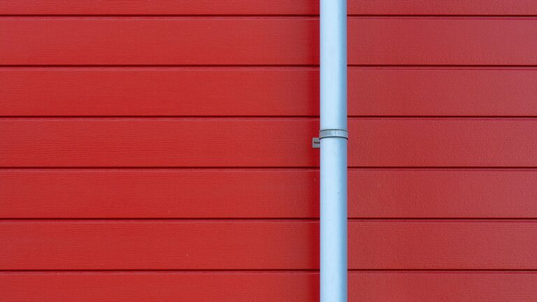 Clean white rain gutter downspout on a red house exterior wall.