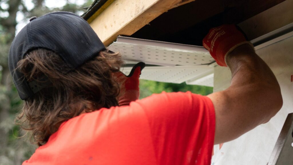 Worker wearing gloves adjusting gutter and soffit at the roof edge.