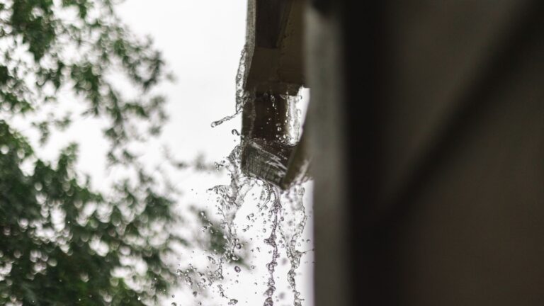 Close-up of rainwater pouring from a house gutter during a heavy rain