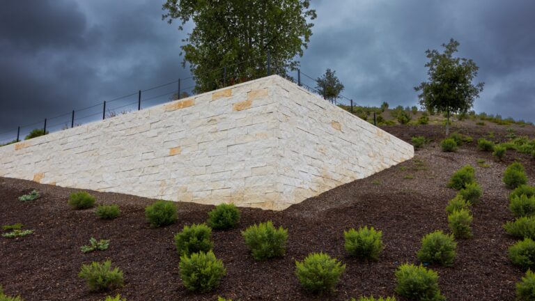 Why Mulch Washes Away on a Slope: What to Consider Mulched hillside bed with young shrubs beside a white stone terrace wall.