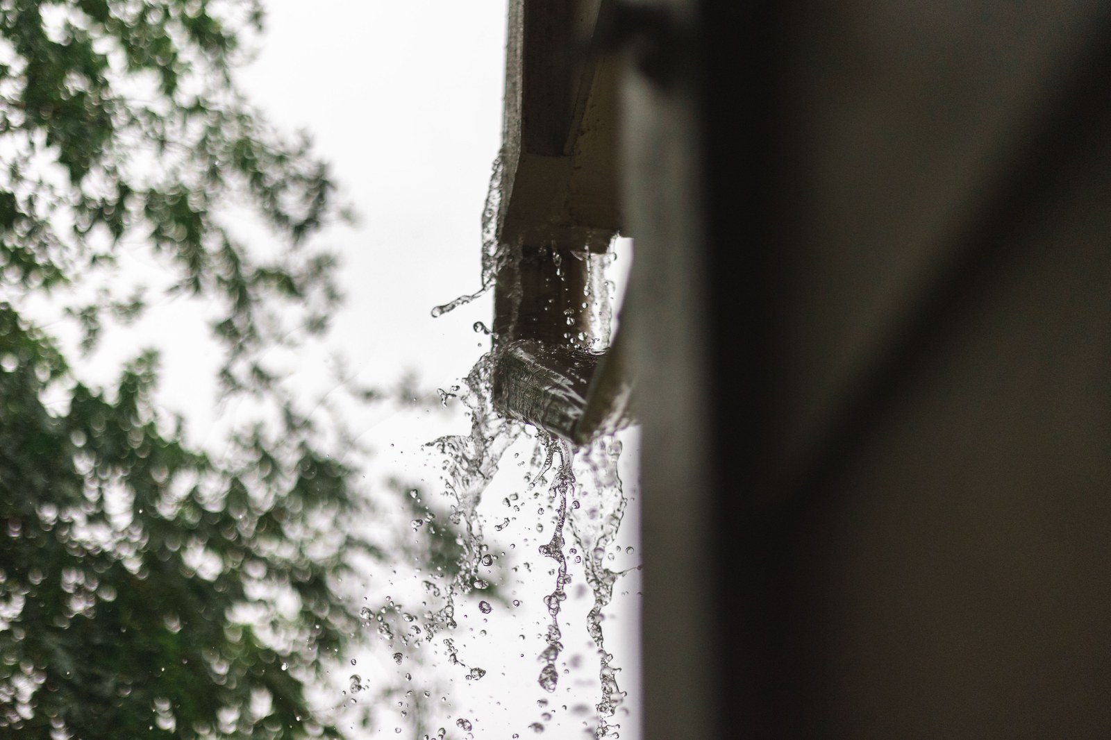 Rainwater pouring out of a gutter during heavy rain.