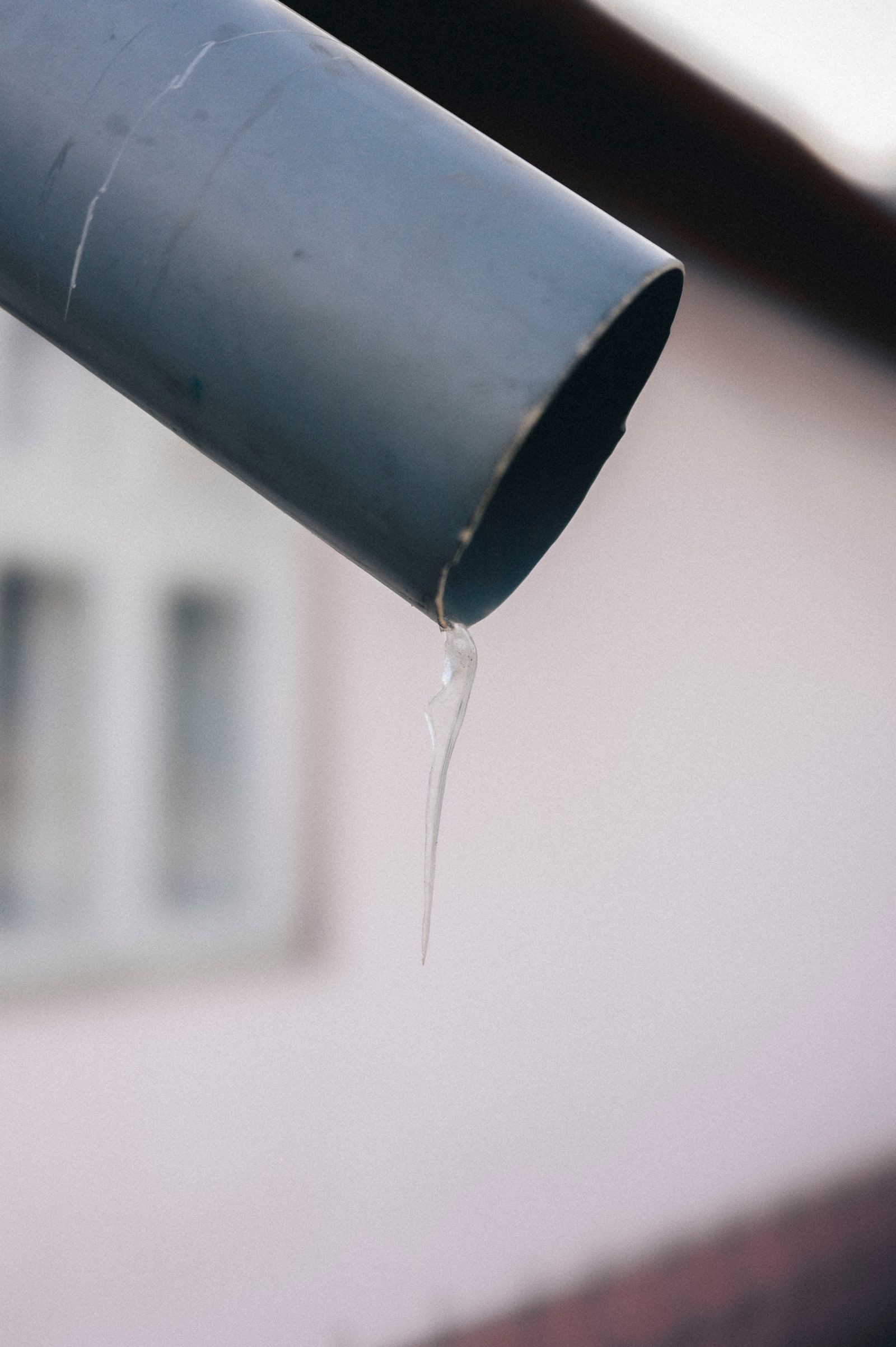 Close-up of an icicle hanging from a metal gutter in winter