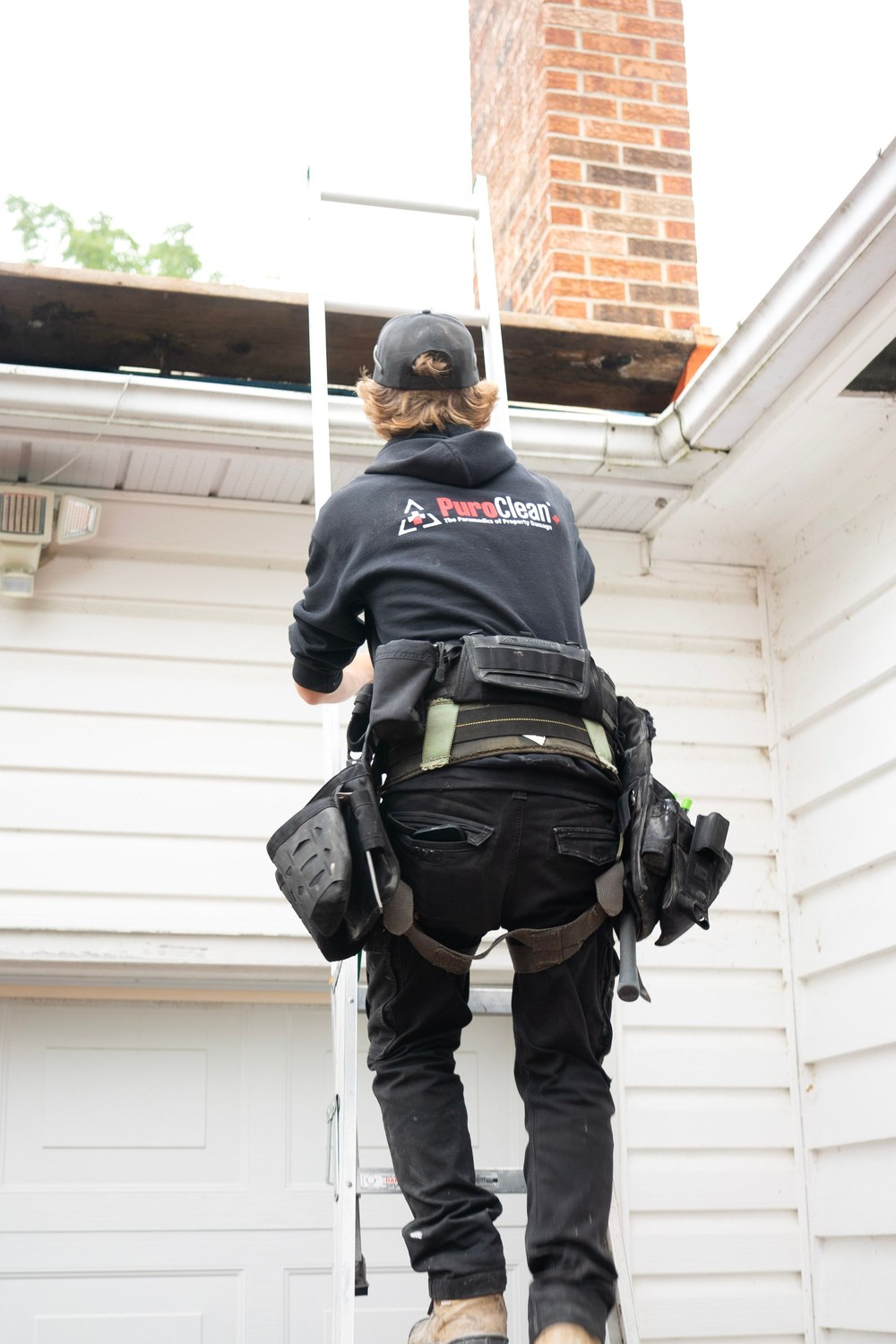 Roofing worker in safety gear climbing a ladder to reach the roofline for exterior maintenance work