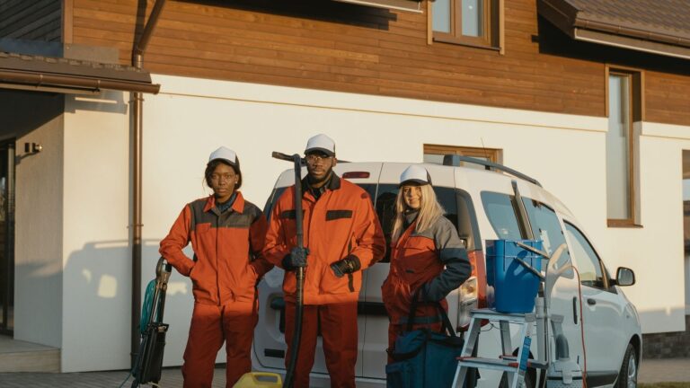 Exterior cleaning crew in orange uniforms with equipment standing in front of a house