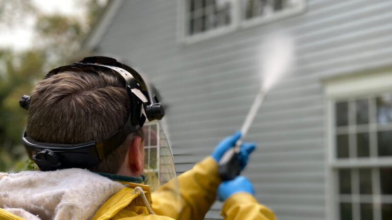 Professional in a yellow raincoat pressure washing a home exterior with a spray wand