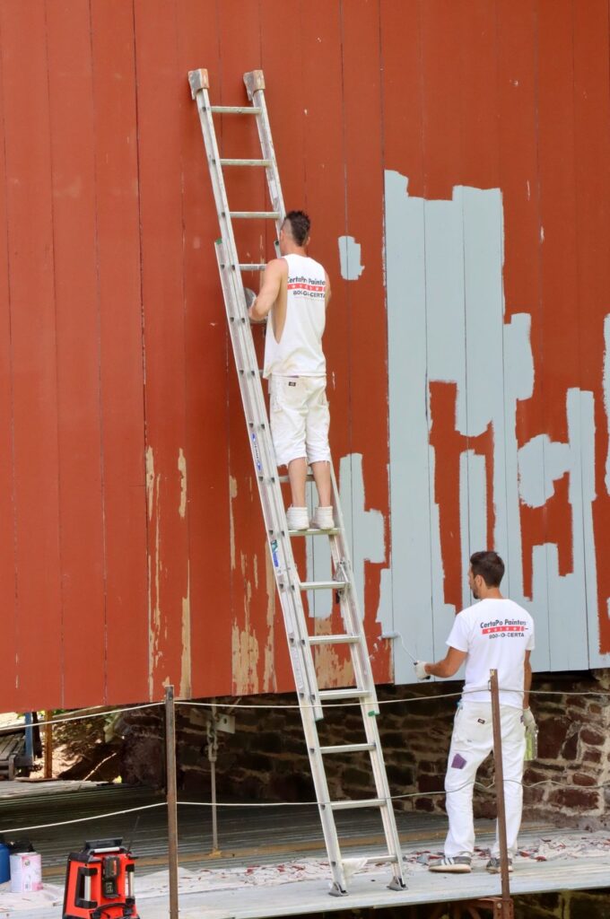 Two painters repainting an exterior wall from an extension ladder