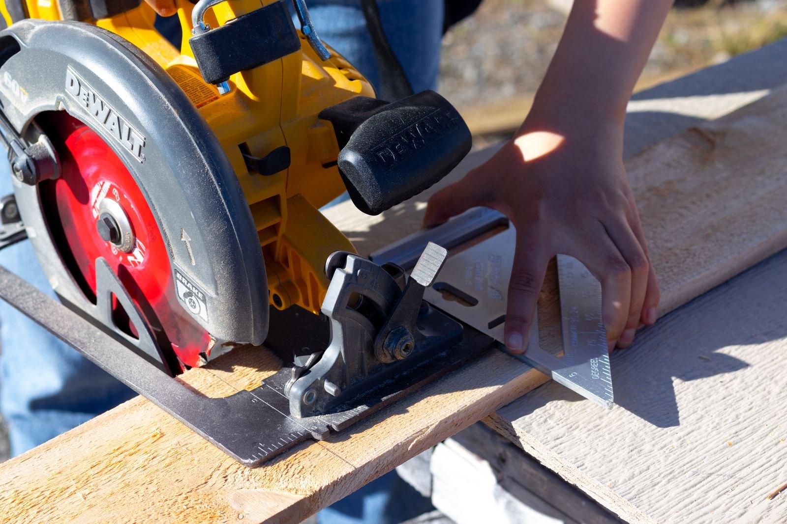 Close-up of a worker cutting a board with a circular saw, guided by a speed square